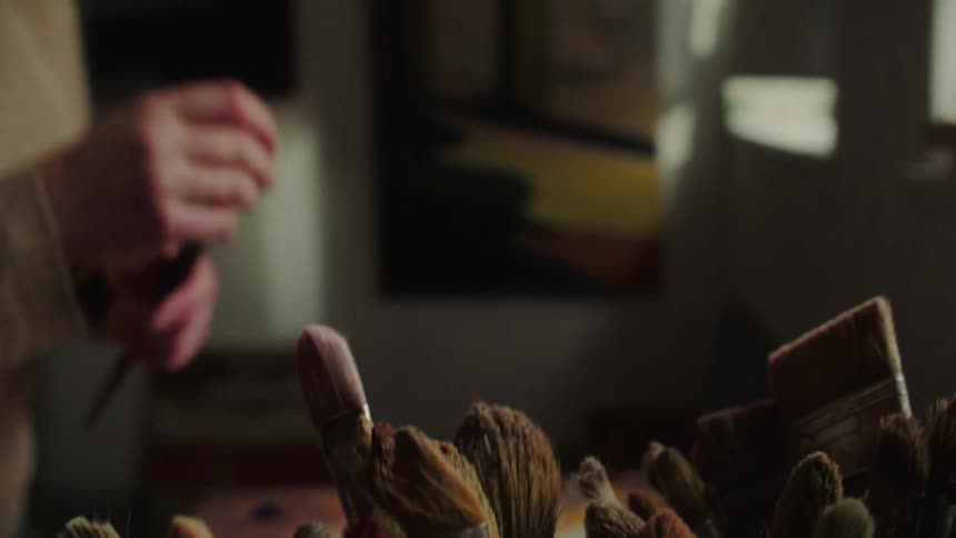 Woman in an art studio during the daytime selects a few paintbrushes
