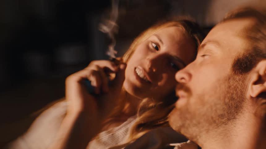 Woman smoking a joint held by boyfriend as they lounge on couch
