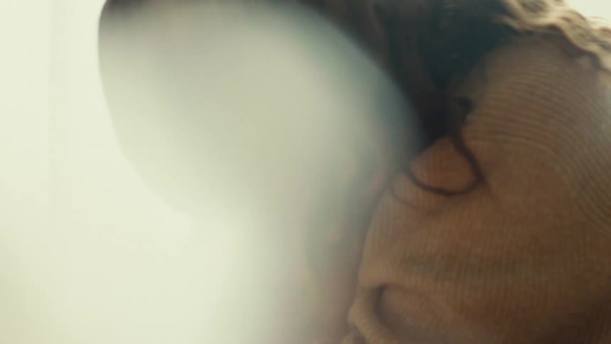This is an extremely closeup softfocus shot of a persons profile possibly hugging someone or wearing a scarf the image is mostly obscured by a bright white or hazy light flare making the details indistinct