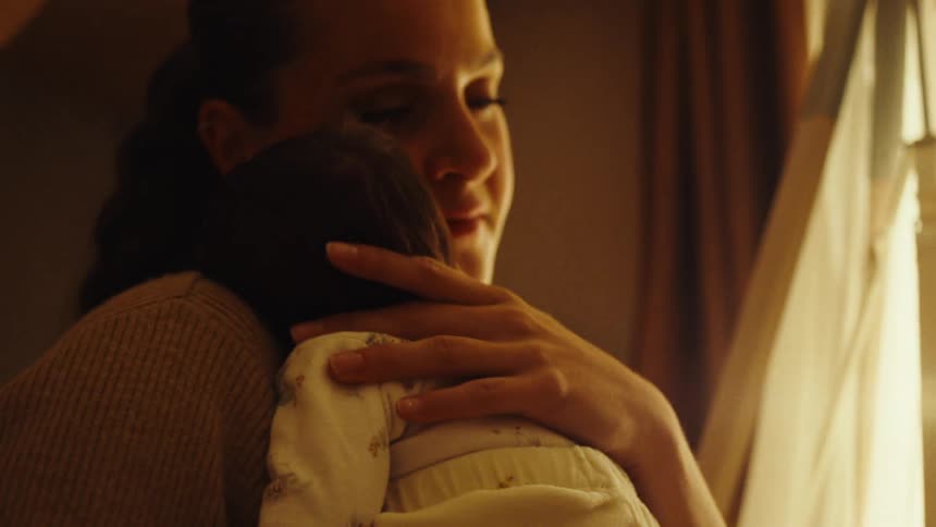 Mother tenderly cradles a baby close to her chest in a bright sunlit room