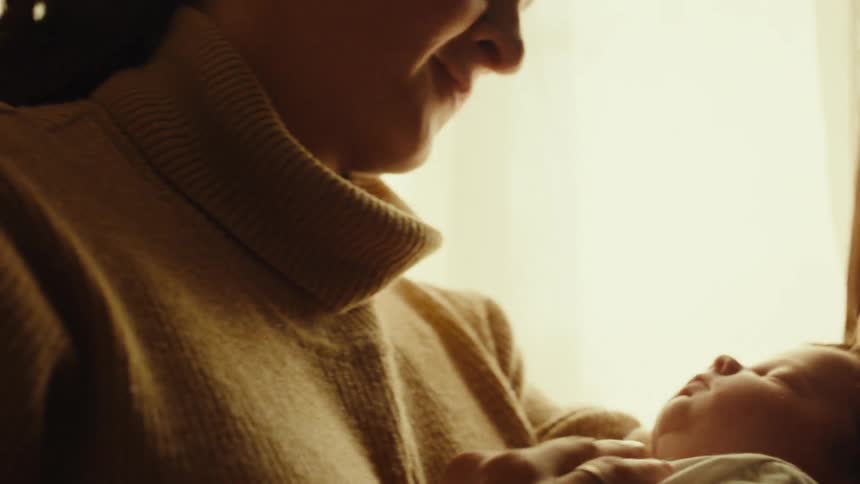 Closeup of a mother gently holding and embracing her newborn indoors