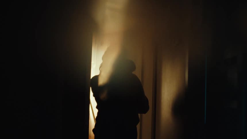 Silhouette of a woman carrying a baby in a hallway lit by bright backlight
