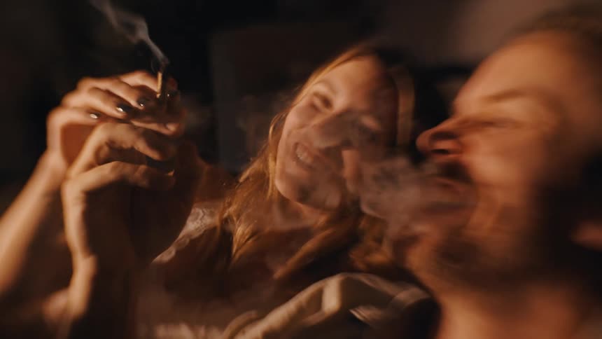 People smoking a rolled cigarette while exhaling smoke in a warmlit setting