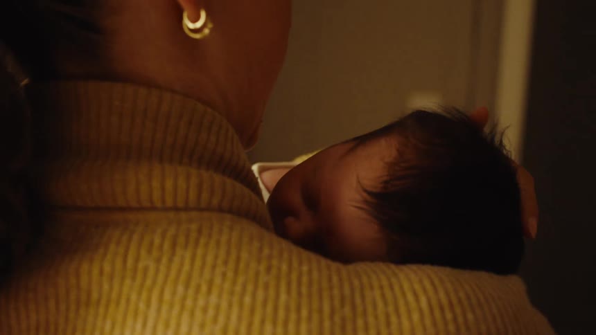 Woman holding a baby resting on her shoulder under warm light