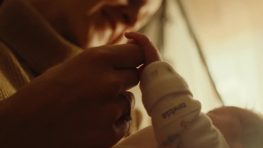 A mother carries her baby smiling warmly as she plays with the babys fingers