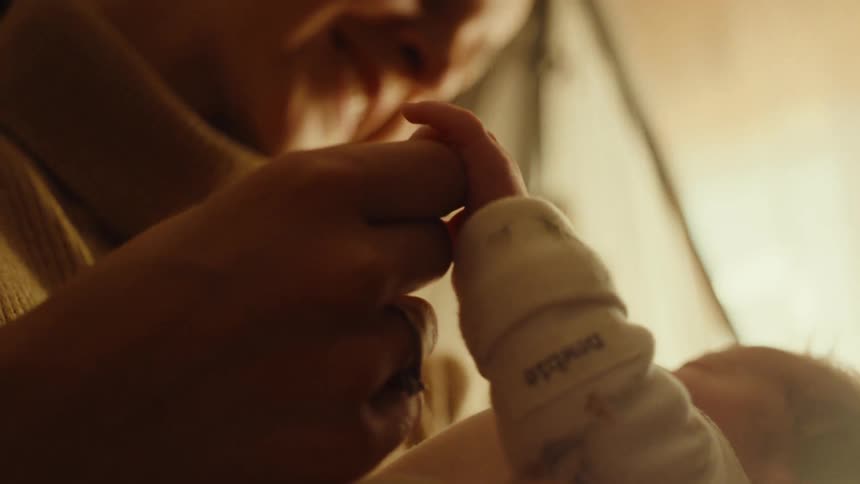 Closeup of an adult gently holding a newborns tiny hand in warm indoor light
