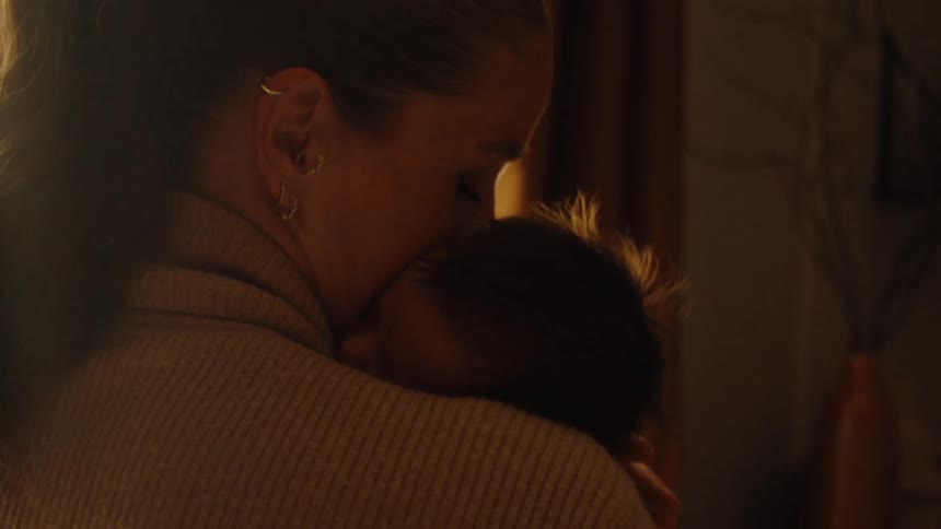 Young adult woman holding and kissing a baby in her arms indoors during day time