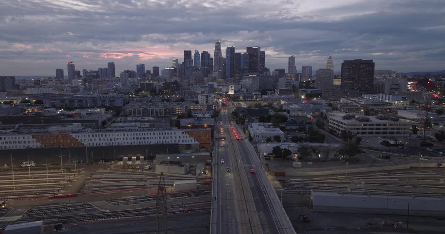 Aerial wide shot of the Los Angeles skyline at dusk with a busy bridge over an industrial rail yard