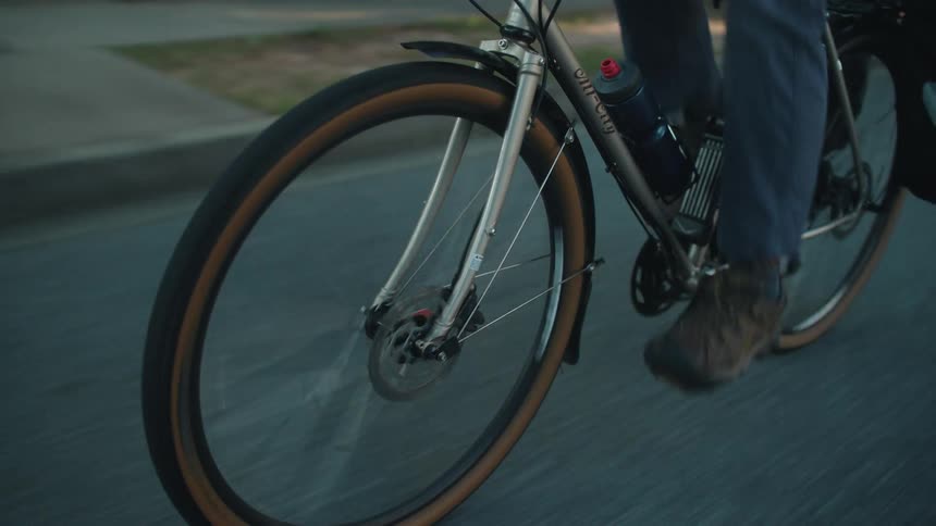 A closeup shot focuses on the front wheel of a bicycle as it rapidly spins showing the cyclists foot pedaling while riding smoothly along a paved road
