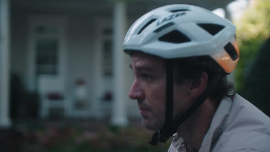 A man wearing a helmet rides his bike along a residential street