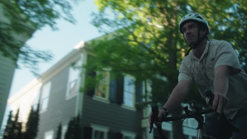 Man riding his bicycle past houses and cars on a neighborhood street