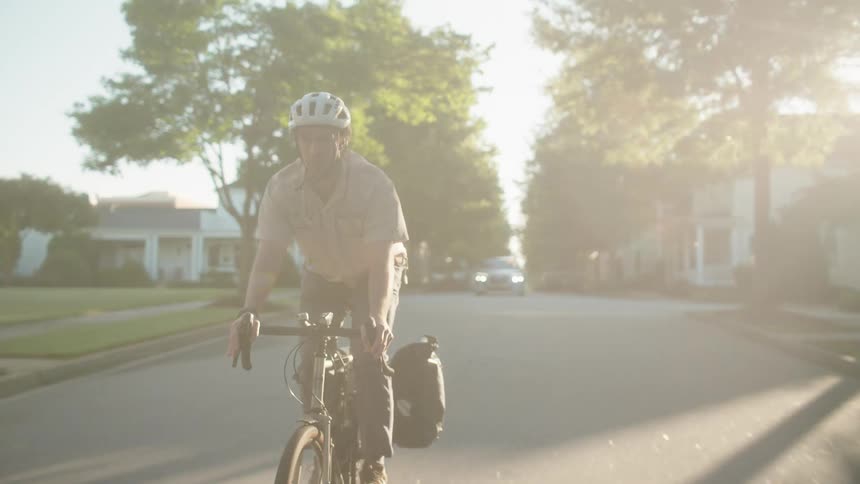 A young man wearing a helmet cycles through a residential neighborhood at midday