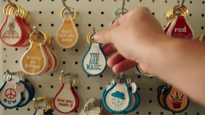 Closeup of a hand picking a keychain from a pegboard of humorous or uplifting keychains