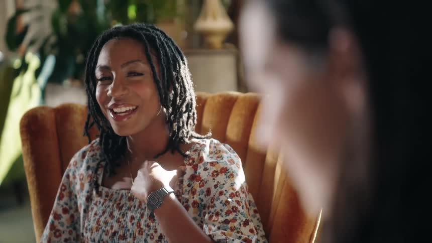 Young black woman sitting on an armchair talking with a young white woman in a living room indoors during day time