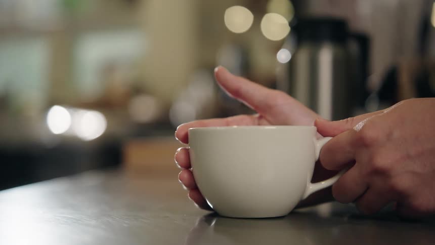 Close up of a woman lifting a coffee cup from a table in a cafe during daytime