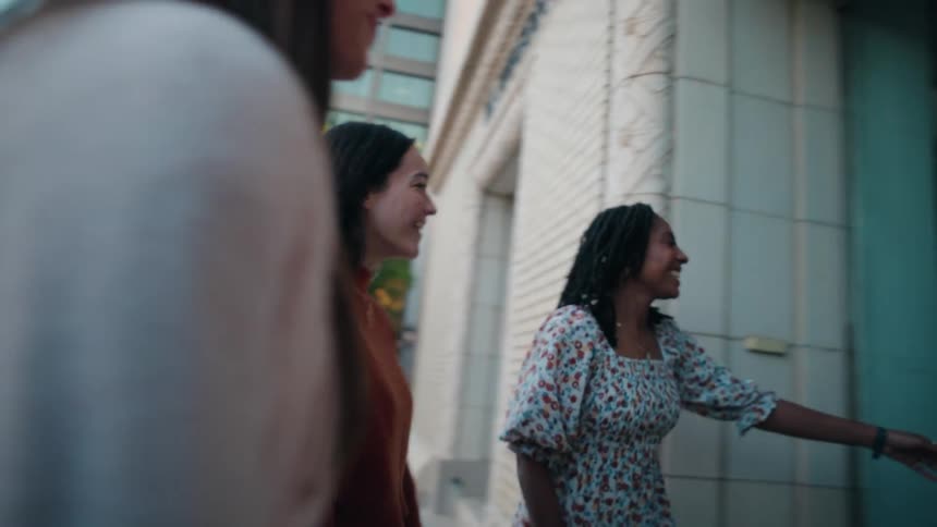 A group of female friends enter a large building in a metropolitan city during daytime
