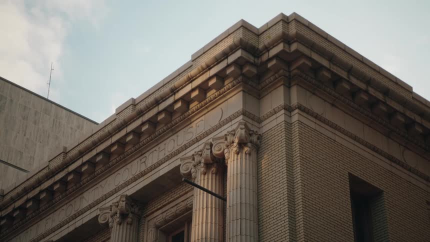 Classical style county courthouse with detailed columns stands against a bright sky
