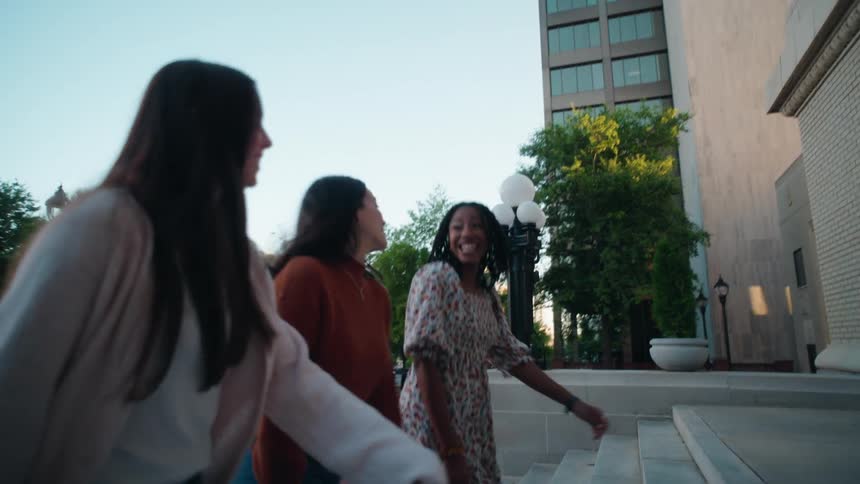 Three women walking up outdoor steps while talking and laughing at dusk