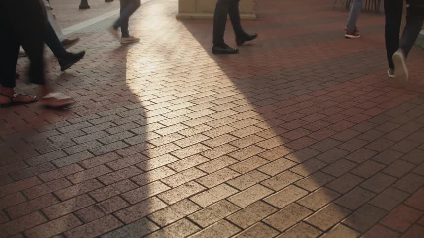 People walk along a tiled street in the city on a sunny day