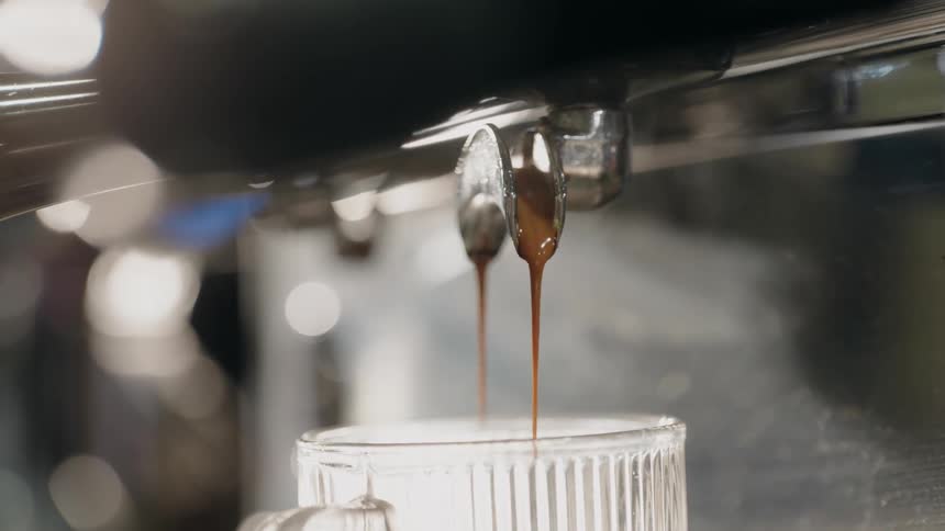 Coffee is dripping from a machine into a clear ribbed glass