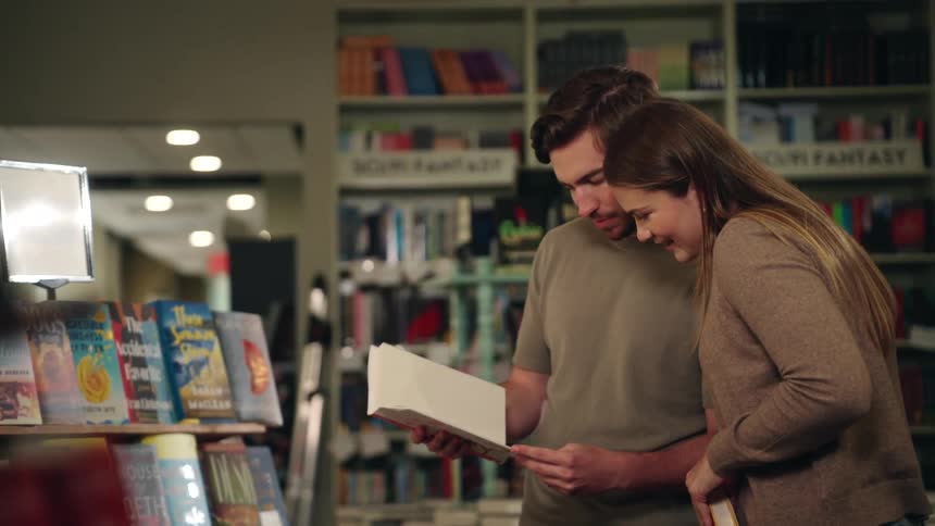Friends reading a selected book while standing at a shelf in a book library