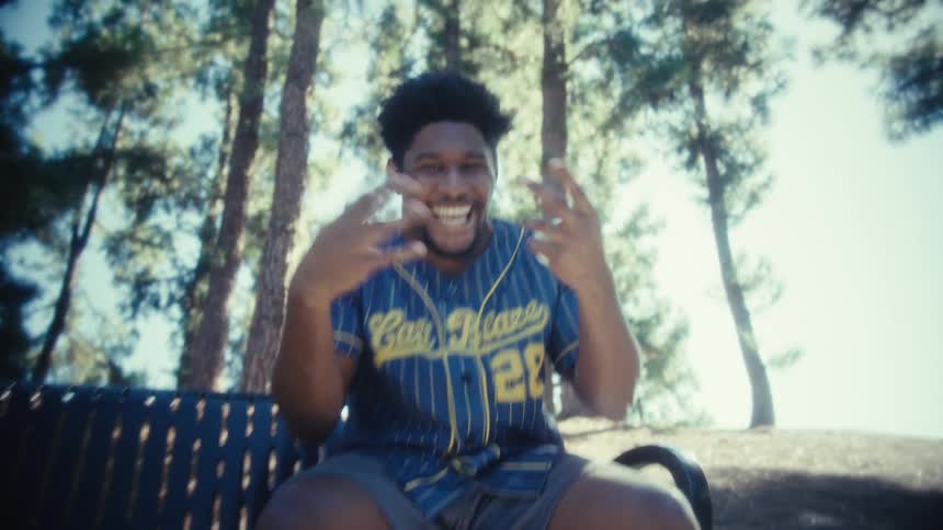 A young black man laughing and celebrating while sitting on a bench outdoors during daytime