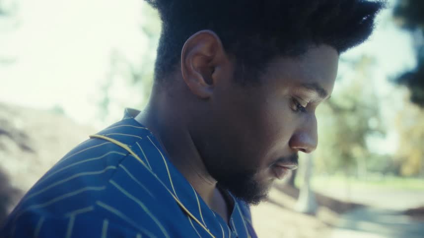 Man wearing a blue sports jersey looking down in a treefilled outdoor area