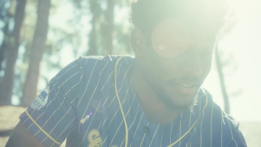 Person in blue pinstriped shirt with yellow accents smiles under sunlight among tall trees