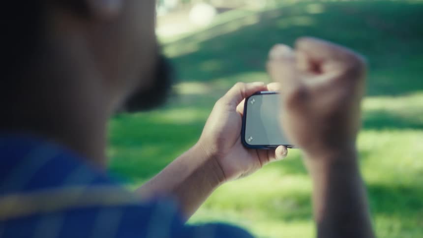 Person holding a smartphone horizontally while watching a celebration outdoors