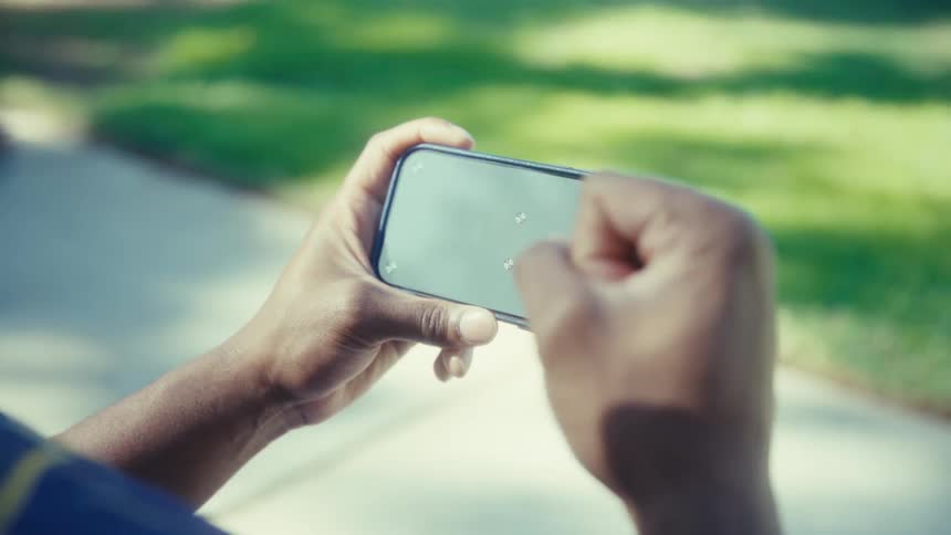 The man pumps his fist while holding a cell phone on a sunny day