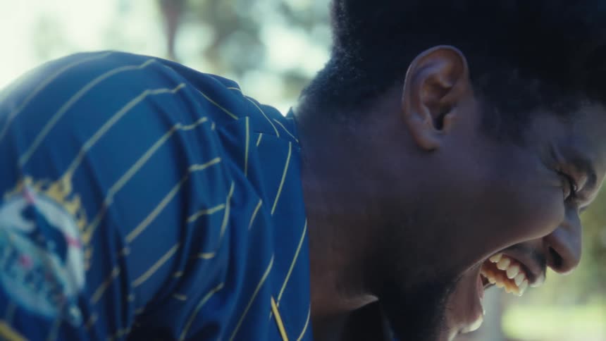 A black man sits outdoors while looking at his smartphone with excitement