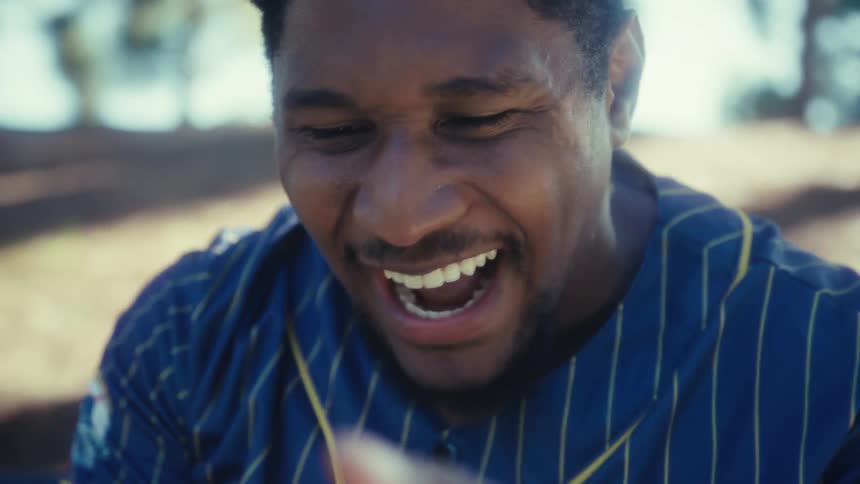 A man is celebrating as he sits in a park looking at his cellphone