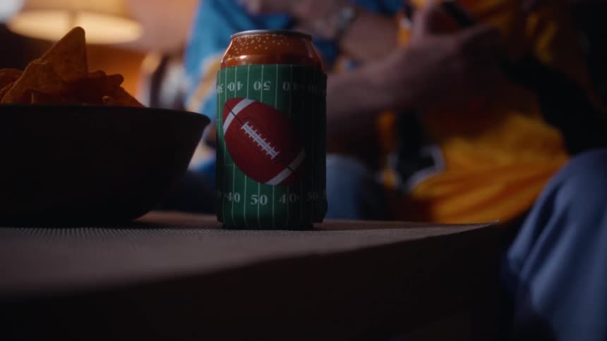 Elderly couple in football jerseys chats cheerfully in lit room with snacks on the table