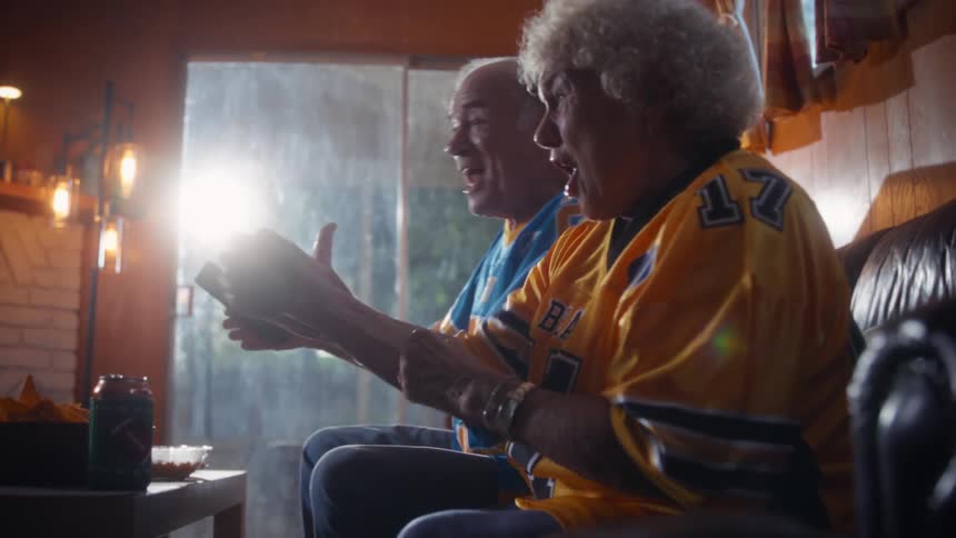 Elderly couple cheers and smiles while sitting in their living room and watching a competition