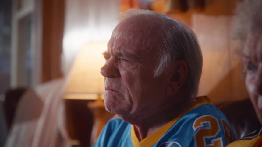 Elderly man and woman with concentrated expressions watching television