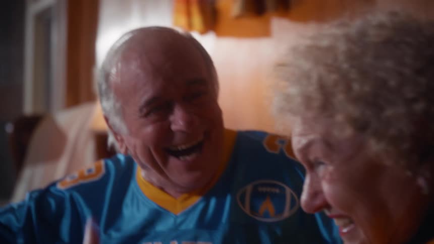 Older couple in colorful sports jerseys sitting side by side in an indoor setting
