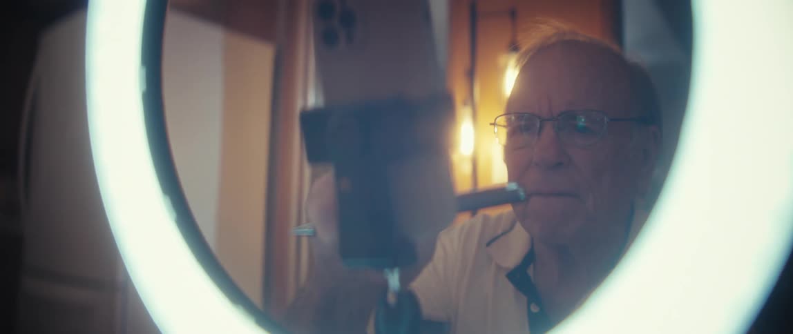 Elderly man makes selections on the smartphone held in a framework standing in front of a ring light