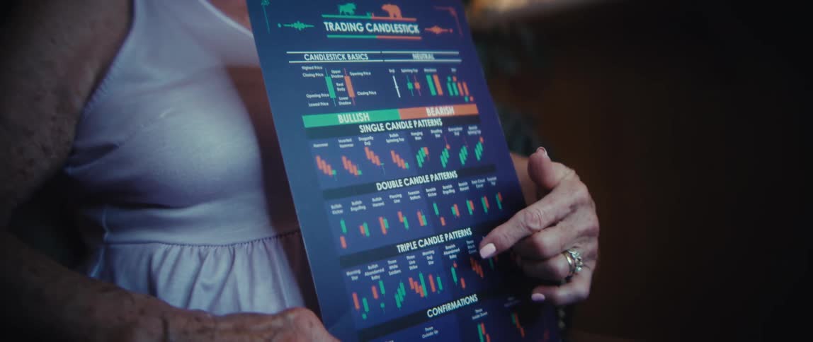 An elderly woman holding a financial chart excitedly talks to an older man wearing glasses and a white polo shirt in a dimly lit room