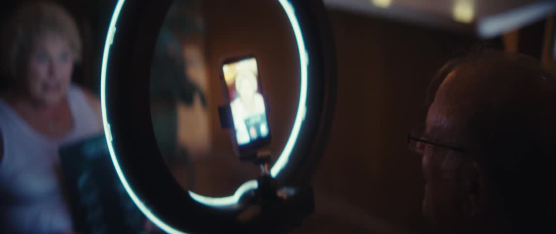 Elderly woman being recorded by a smartphone on a ring light while presenting printed material