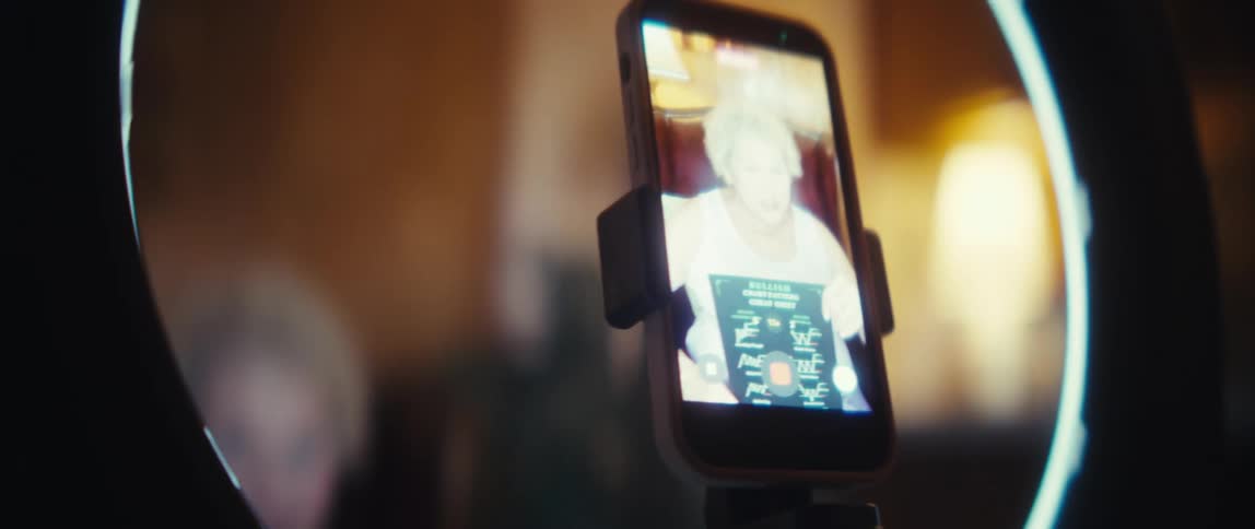 Older woman reading a paper in front of a ring light with a phone recording in an indoor setting