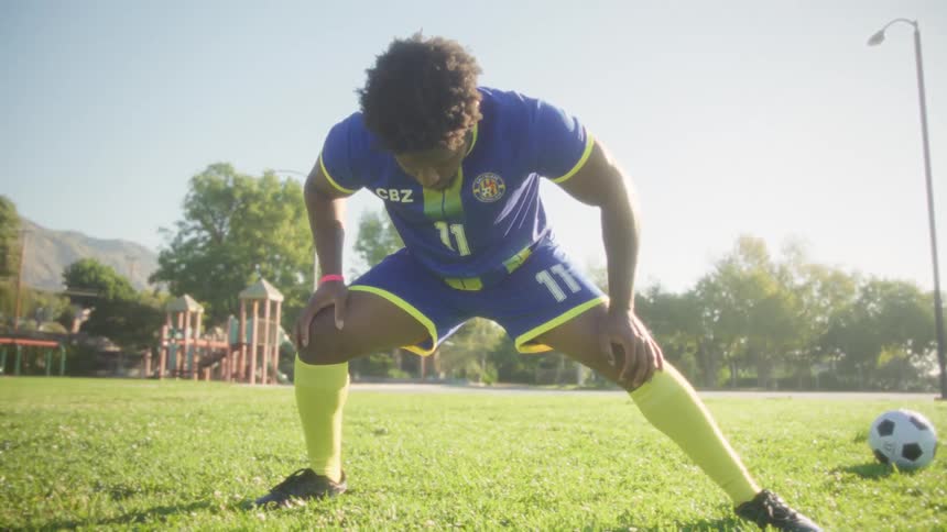 A soccer player wearing a blue uniform stretches on the field