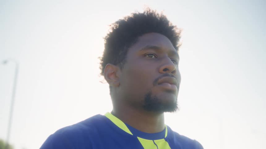 Man in blue and yellow sports shirt faces sideways under bright sun with overexposed background