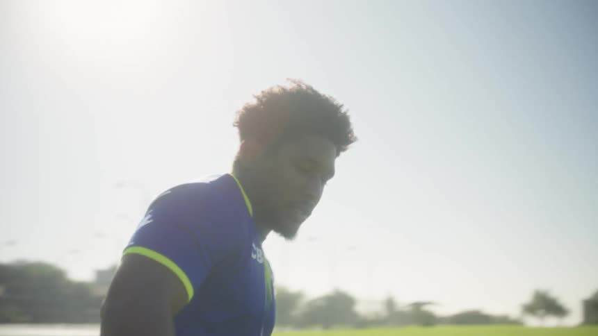 The video opens with a man in a blue and yellow soccer uniform number 11 practicing on a grassy field with a soccer ball and orange cones the camera quickly zooms in to a closeup showing the mans determined expression under bright sunlight before he