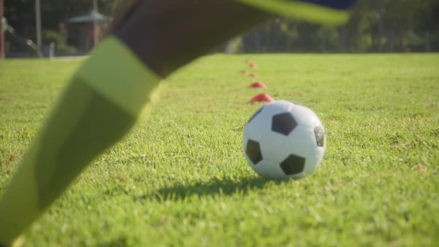 Player stretching near the soccer ball on a sunlit field