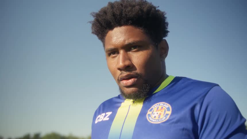 Close up of a young black male player taking a stance while playing soccer on an outdoor field during daytime