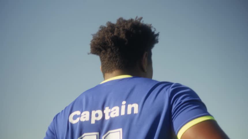 Wearing a blue number eleven jersey the team captain walks confidently forward with a soccer ball tucked under his arm beneath a clear bright sky