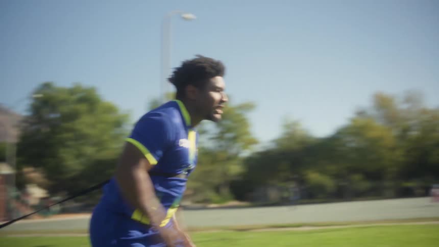 A man sprints across a grassy field with a resistance parachute with mountains in the background