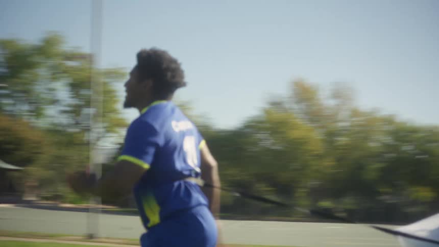 Team captain of a soccer team runs across a field close to a residential area located near the mountains while dragging a chute