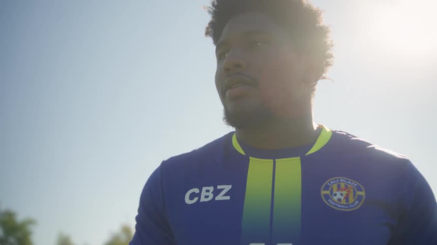 A soccer player stands on a sunny football field wearing a cbz jersey with 11 and captain on the back