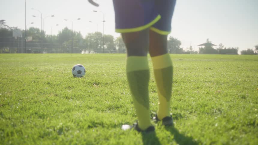 Person in blue and yellow uniform faces ball on grassy field under bright sunlight